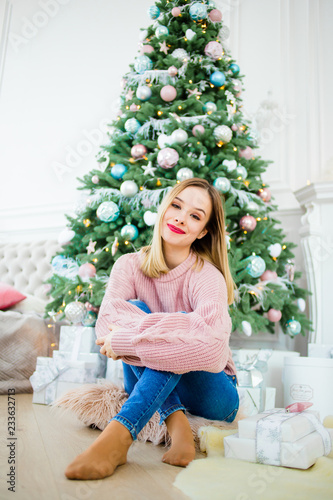 Stunning girl in a pink sweater sitting near a Christmas tree