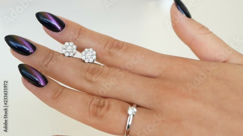 Woman holds earrings with diamonds between fingers and looking on it at her hands. lady trying on some jewel at the boutique.
