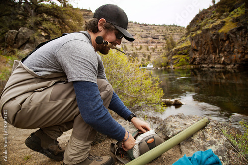 Hiker preparing fishing rod while crouching at lakeshore