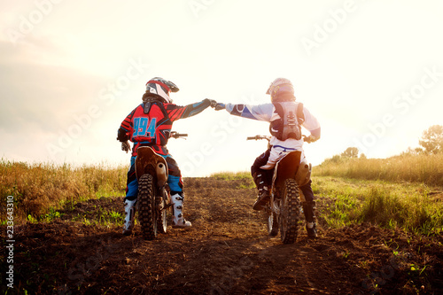 Fotografía Rear view of dirt bikers bumping fists on field against sky