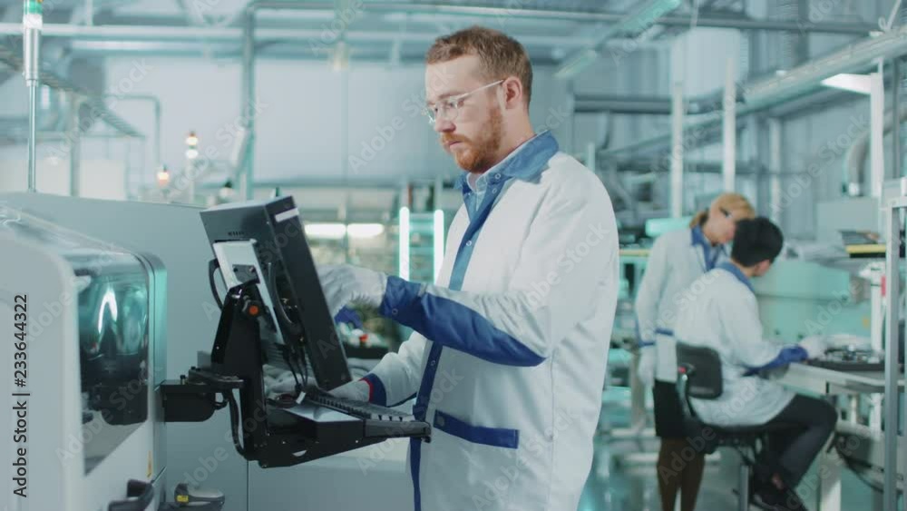 On High-Tech Factory Male Engineer Uses Computer for Programing Pick and Place Electronic Machinery for Printed Circuit Board Surface Mount Assembly Line. Production of PCB with SMT Machinery. On High-Tech Factory Male Engineer Uses Computer for Programing Pick and Place Electronic Machinery for Printed Circuit Board Surface Mount Assembly Line. Production of PCB with SMT Machinery.