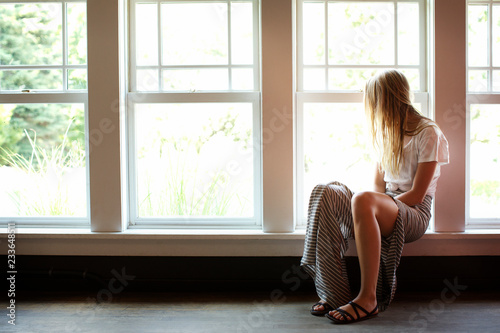 Fotografija Woman looking away while sitting on window sill at home