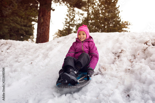 Fotografi Happy girl tobogganing on sled at snowfield