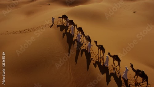 Aerial drone of a convoy of camels with owners across desert sand