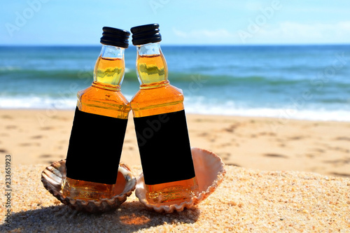 Two little bottles  whiskey in the ocean shells stand on the sand. Alcoholic party in a nautical style on the shores of the Atlantic Ocean.