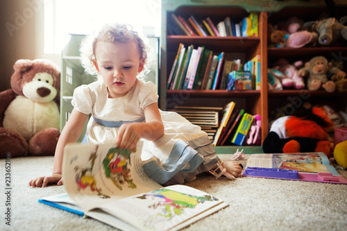 Cute girl reading picture book while sitting on floor at home