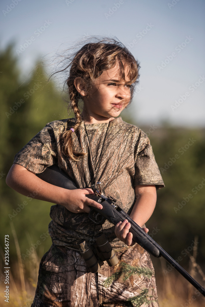Fototapeta premium Girl in camouflage clothing holding rifle while standing on field
