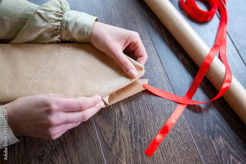Hands of beautiful young woman wrapping present in brown paper and red ribbon