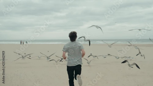 The boy happy man male tourist runs along the beach lake promenade and chases pigeons seagulls gulls birds ocean freedom . photo