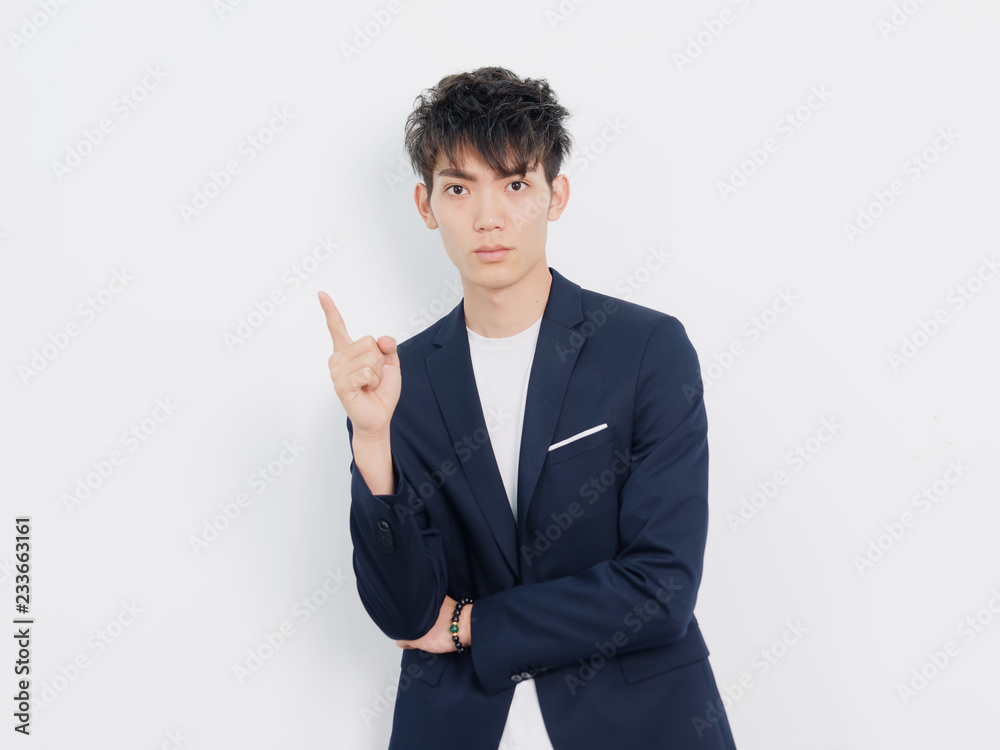 Portrait of handsome Chinese young man in dark blue leisure suit posing against white wall background. Making first gesture with his index finger. Portrait of handsome Chinese young man in dark blue leisure suit posing against white wall background. Making first gesture with his index finger.