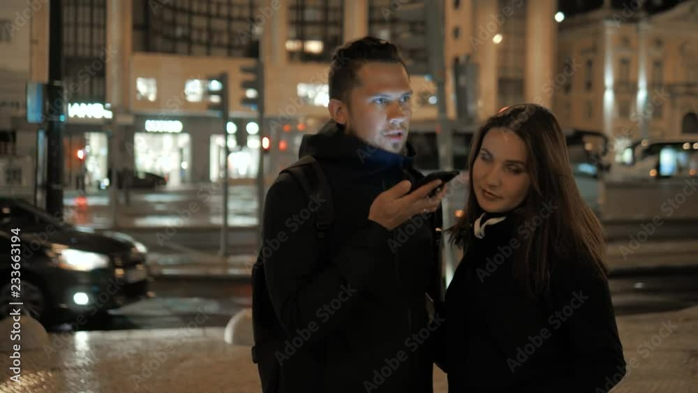 Man and woman couple voice recognition with smart phone near cafe restaurant waiting order, student male use message audio helper finder night city center Man and woman couple voice recognition with smart phone near cafe restaurant waiting order, student male use message audio helper finder night city center