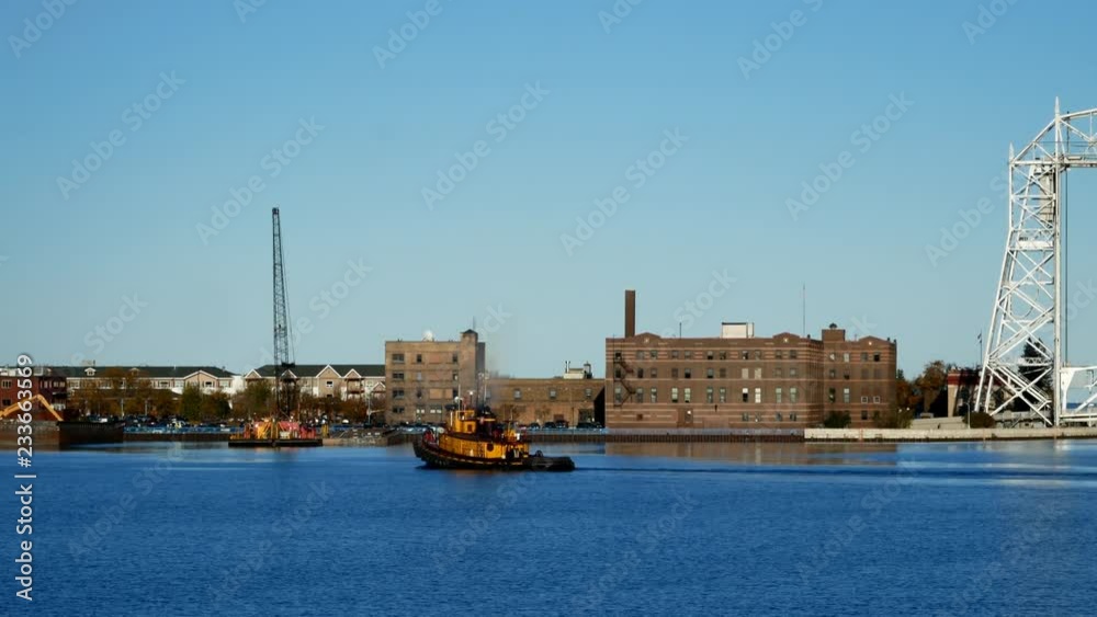 Yellow tug boat sails in Duluth Minnesota Harbor near the iconic aerial lift bridge on a sunny afternoon Yellow tug boat sails in Duluth Minnesota Harbor near the iconic aerial lift bridge on a sunny afternoon