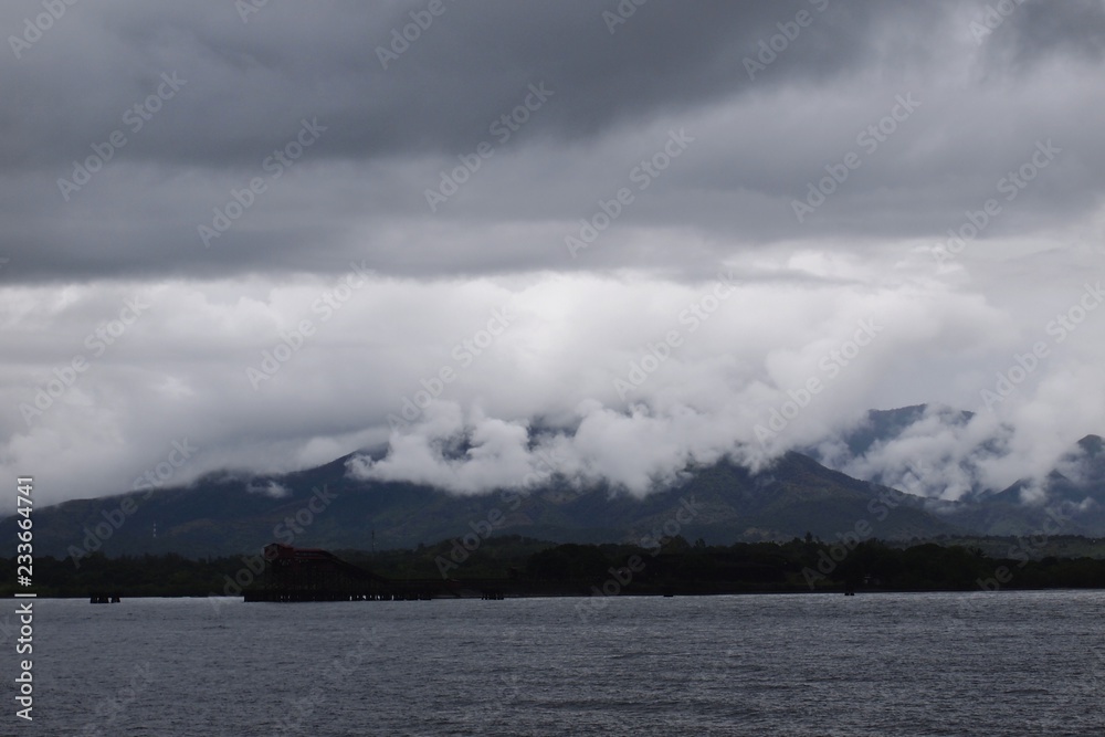 Sea view of Dark downcast moody sky with white clouds over hills 
