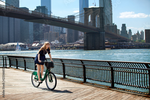 Obraz na plátne Woman cycling on promenade against Brooklyn Bridge