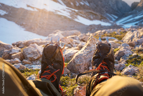 Low section of man in crampon shoes relaxing on cliff