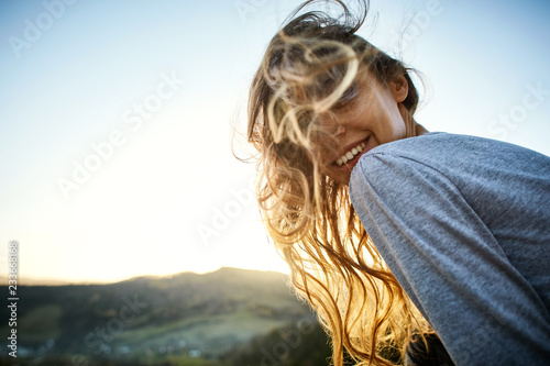 portrait of smiling cheerful woman with long hair sitting on edge of cliff against background of sunrise. woman's hair fluttering beautifully in the wind
