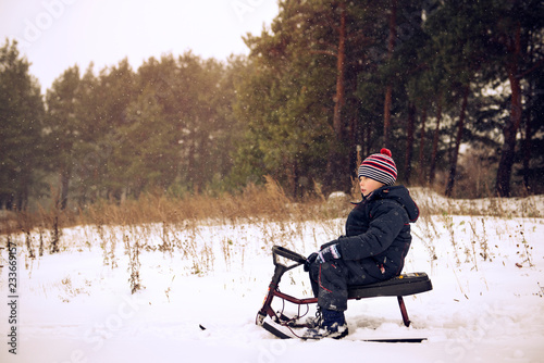 Tablou pe pânză Side view of boy sledging on snow covered field
