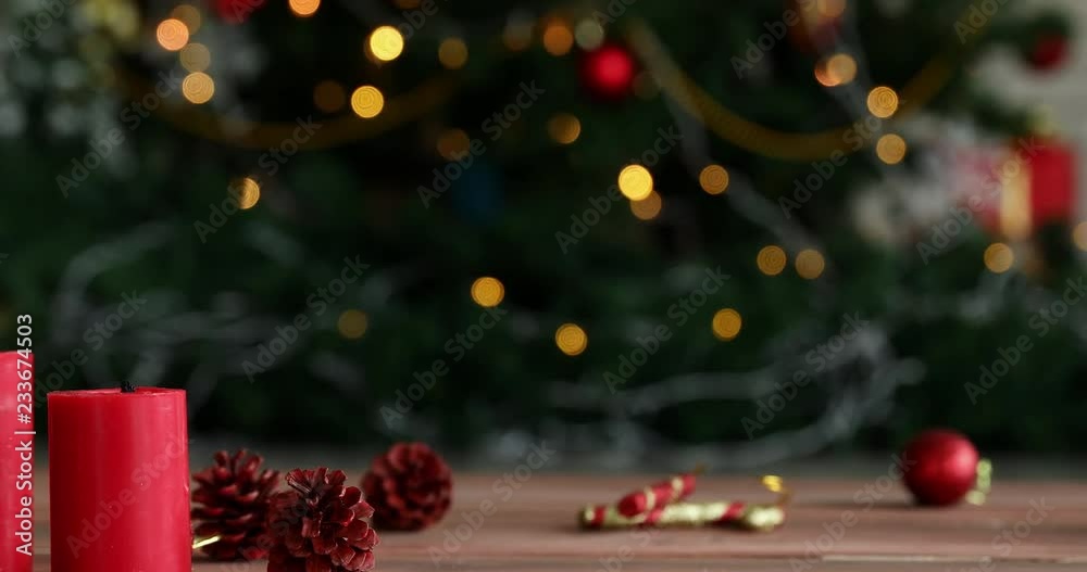 Moving scene, there is ornament on wooden desk, camera panning to left, someone hand light candle, small Christmas tree beside it, blur Christmas tree are background, concept for Christmas festival.