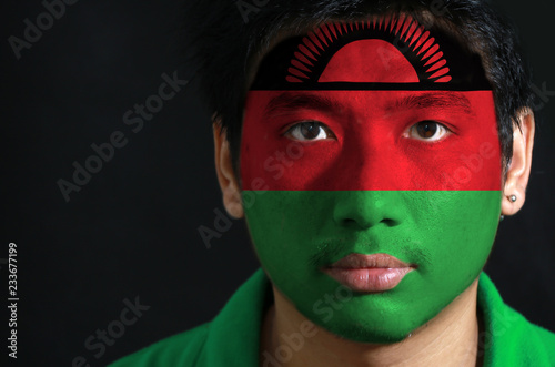 Portrait of a man with the flag of the Malawi painted on his face on black background, black red and green; charged with a red rising sun on black stripe. photo