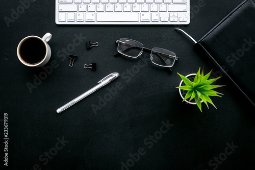 Office desk of chief, director or top manager. Computer keyboard, expensive black notebook, glasses, coffee on black background top view copy space