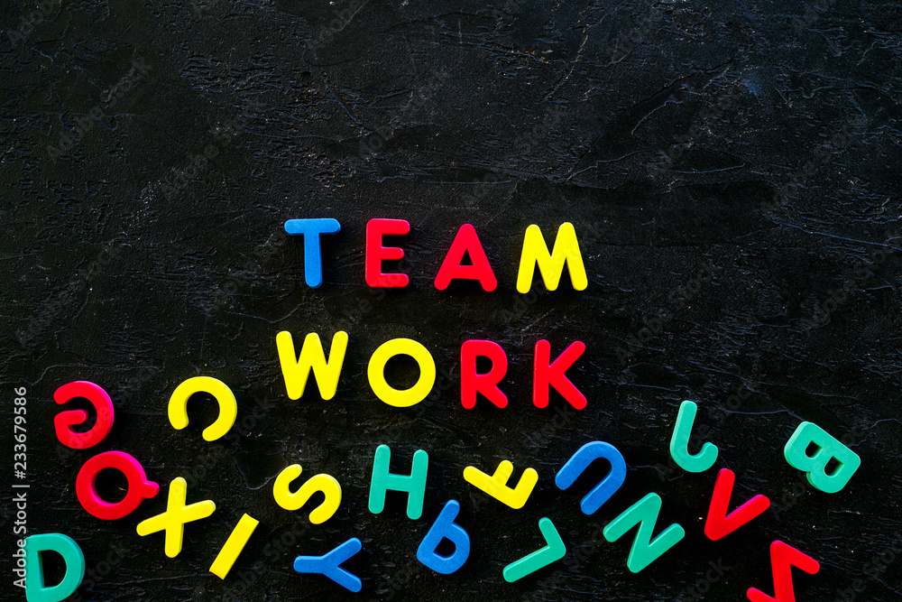Fototapeta premium Teamwork training concept. Text teamwork lined with colored letters near toy letters on black background top view space for text
