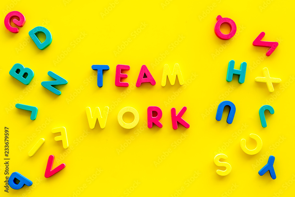 Fototapeta premium Teamwork training concept. Text teamwork lined with colored letters near toy letters on yellow background top view copy space