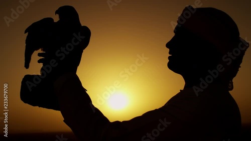 Proud Arab in dishdasha in silhouette at sunrise with his trained falcon photo