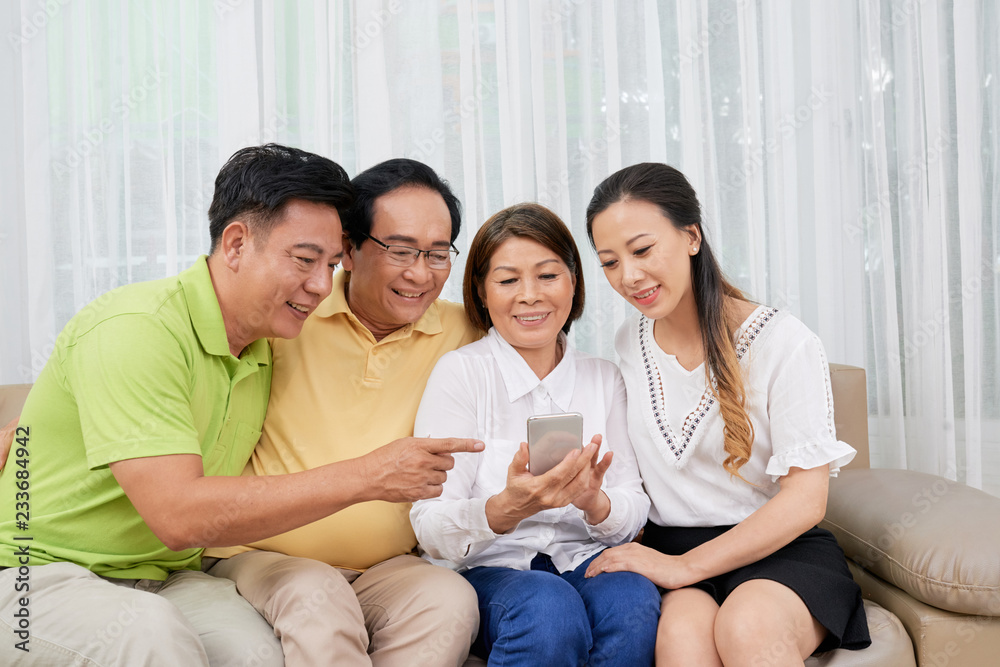Cheerful Asian family looking at photos on smartphone screen