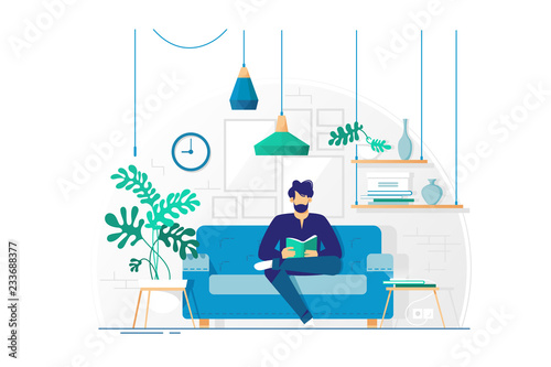 Young man with beard reading book sitting on couch.