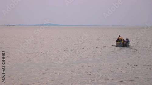 Two fishermen in fishing boat heading out on Lake Victoria from Kalangala, Uganda. Far away islands and horizon in background. Boat moves further away. photo