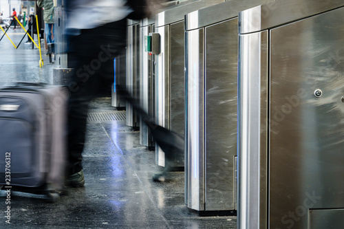 Side view of a man with a rolling suitcase passing through stainless steel ticket gates in a metro station with motion blur. photo