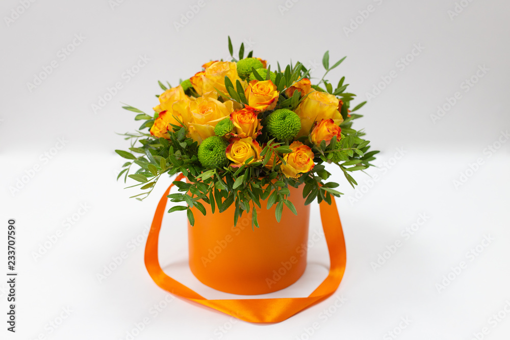 Bright bouquet of orange roses and green flowers in an orange box for hats on a light background