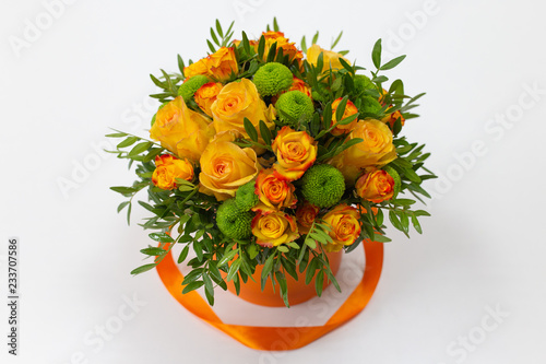 Bright bouquet of orange roses and green flowers in an orange box for hats on a light background