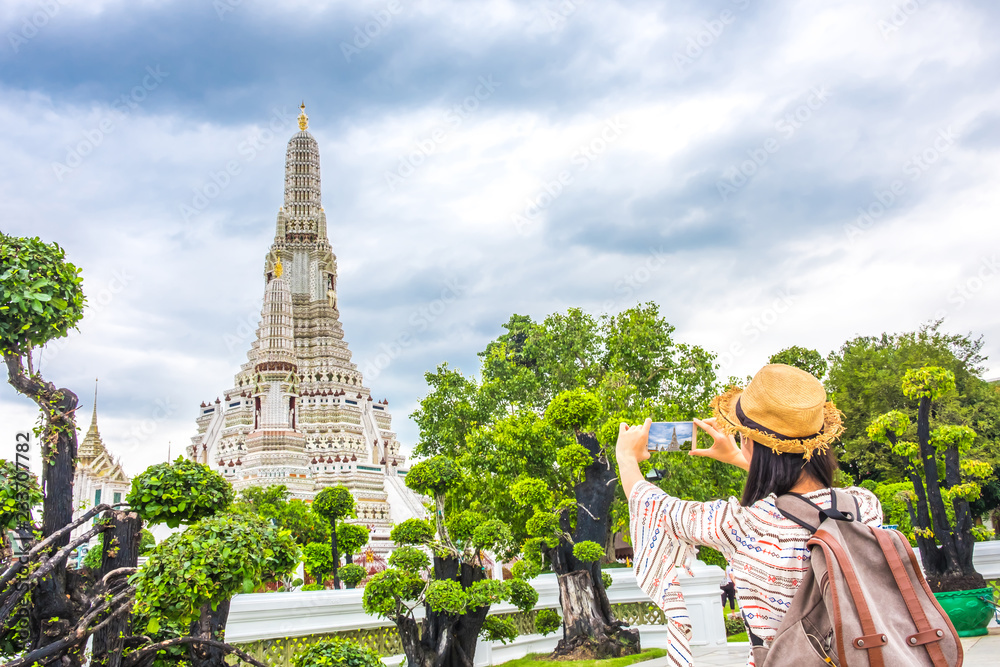 Asian woman tourist with backpack is taking a photo or selfie with smartphone during a travel and relax in holiday at pagoda arun temple It is a landmark and attractions of Bangkok Thailand.
