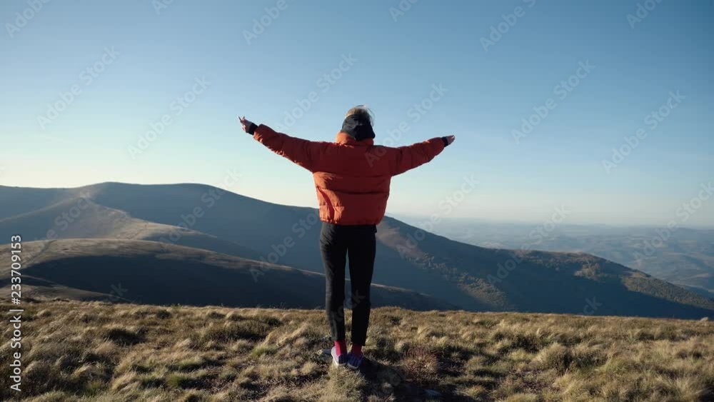 Camera follows hipster millennial young woman running up to road side on top of mountain summit, jumps on top of rocks, raises arms into air, happy and drunk on life, youth and happiness Camera follows hipster millennial young woman running up to road side on top of mountain summit, jumps on top of rocks, raises arms into air, happy and drunk on life, youth and happiness