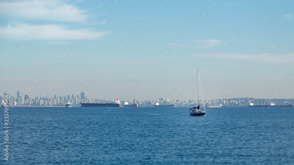 Vancouver skyline with a sailboat and tanker ships on a sunny day.