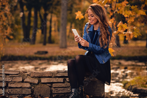 Cute girl using cellphone in park with autumn colors.