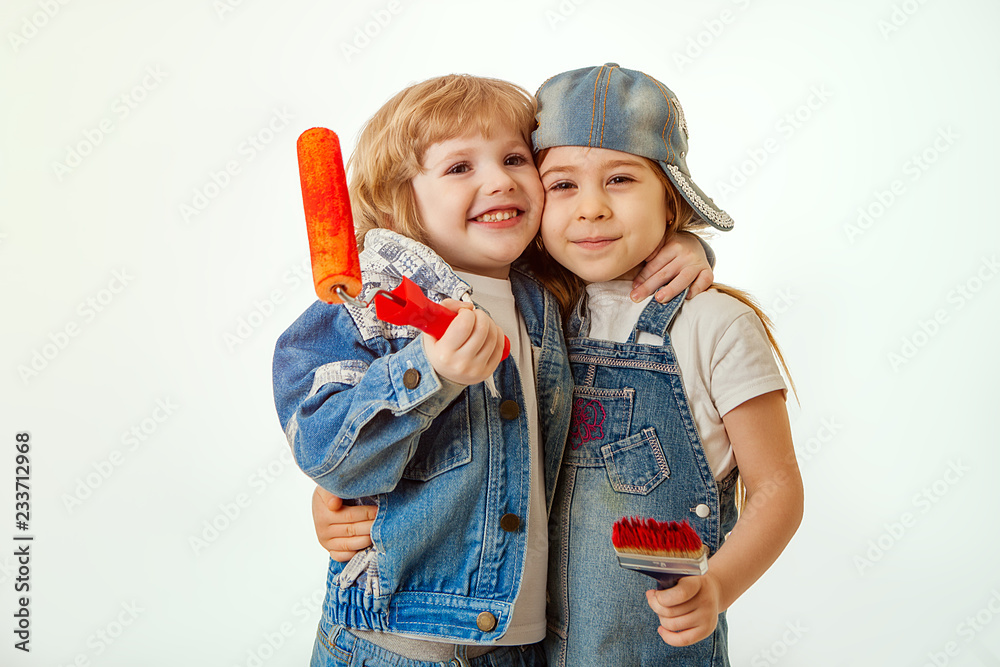 a couple in love, children in denim suits, a boy hugging a girl. In the hands of a paint brush and roller with red paint. Place for text or advertising. Is isolated. a couple in love, children in denim suits, a boy hugging a girl. In the hands of a paint brush and roller with red paint. Place for text or advertising. Is isolated.