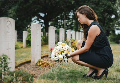 Young widow laying flowers at the grave photo