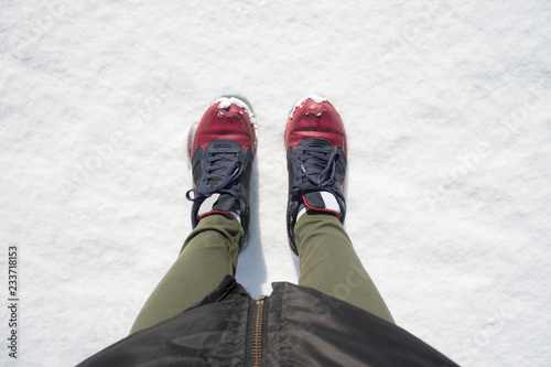 Red and blue women's shoes covered by snow in the winter . Snow background. Top view