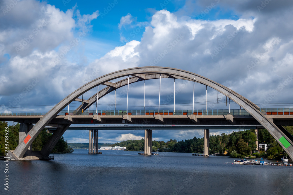 Fototapeta premium Sunny summer view of a arched concrete train bridge with sky, water and boats.