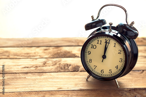 Black clock on an old wooden table, marking twelve o'clock.