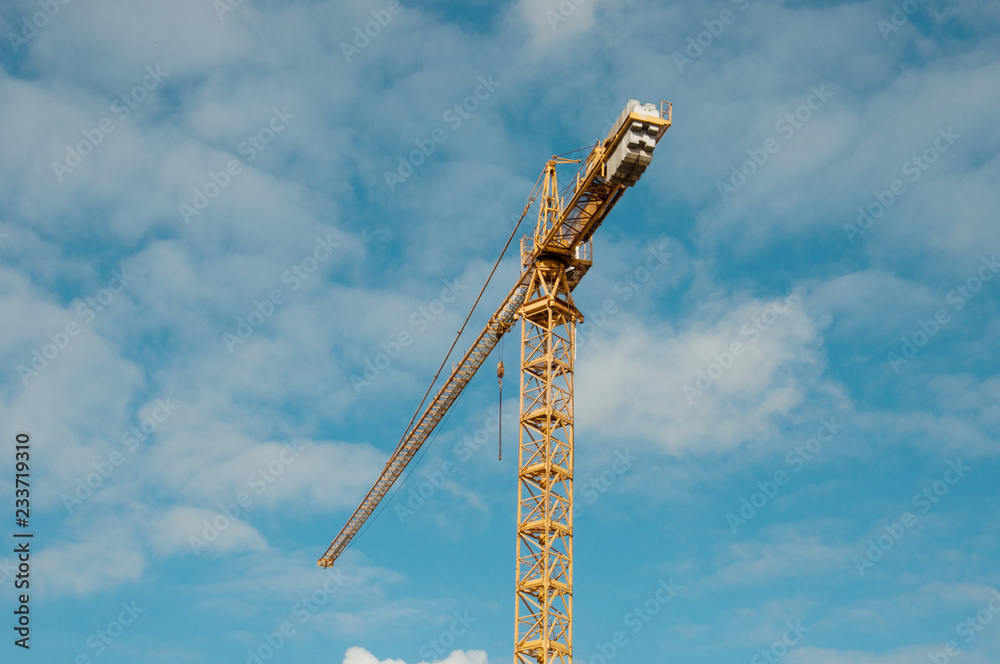 Construction crane tower against a blue sky. Yellow construction crane against the blue sky with clouds Construction crane tower against a blue sky. Yellow construction crane against the blue sky with clouds