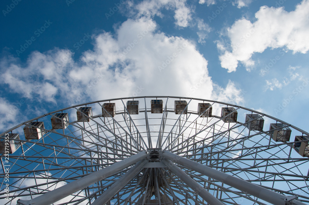 Ferris wheel in an amusement park, view from below look upwards. Sky background with clouds with place for text.