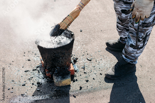 Worker repairs the roof with molten tar from a bucket with a broom. Roof repair tar.