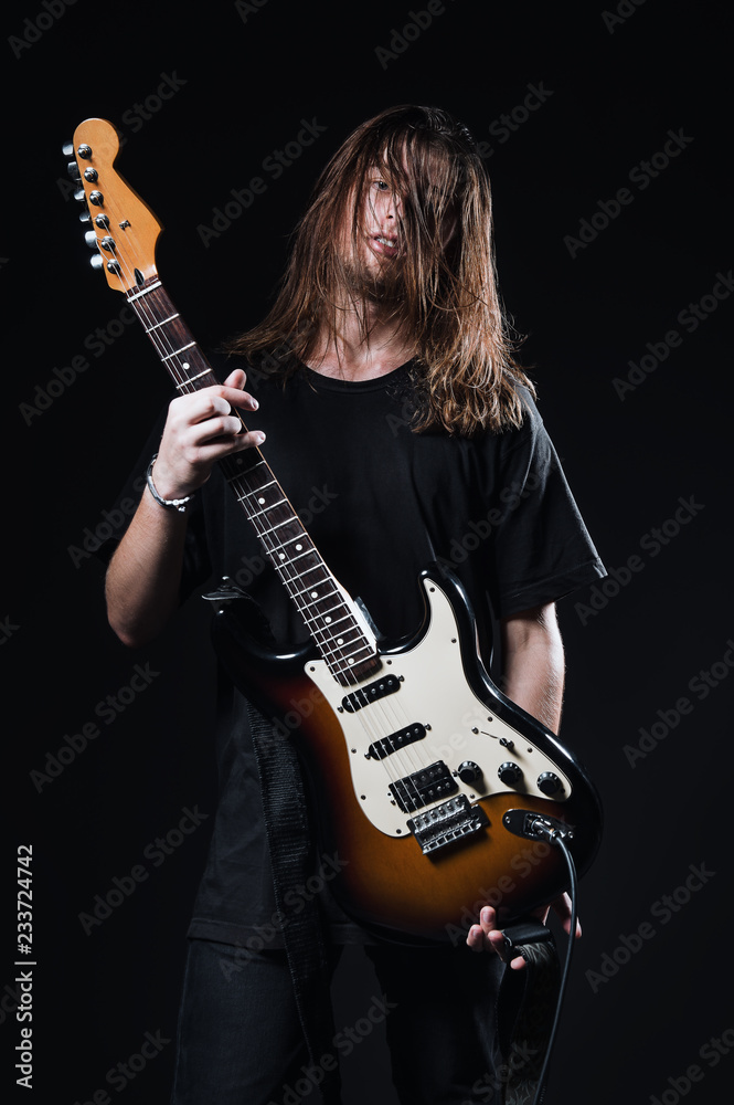 Fototapeta Studio portrait: handsome young man (rock musician) with long hair (rock musician) holds electric guitar in hands