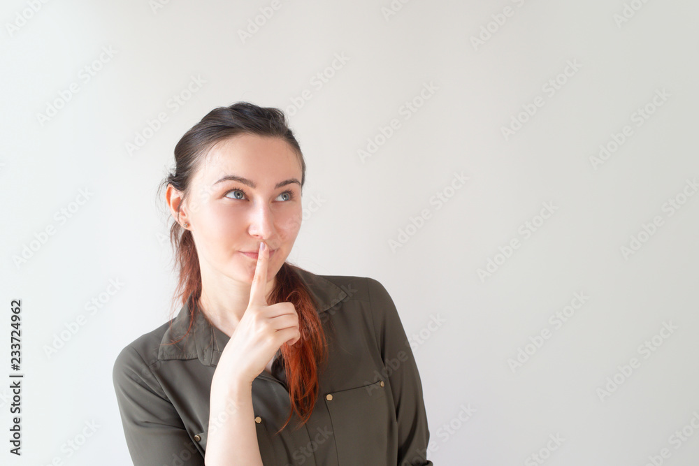 Portrait of happy Caucasian woman holding finger near mouth and smiling. Young female client looking up at copyspace. Wellness and beauty secret concept Portrait of happy Caucasian woman holding finger near mouth and smiling. Young female client looking up at copyspace. Wellness and beauty secret concept