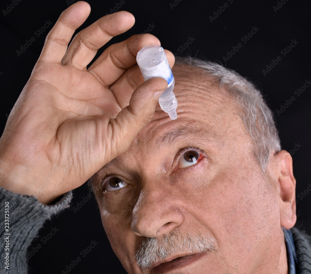 Obraz premium Senior man dripping a red bloodshot eye with eye drops