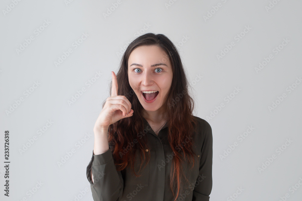 Positive pretty Caucasian girl with big smile raising one finger. Young startuper having bright idea. New project concept Positive pretty Caucasian girl with big smile raising one finger. Young startuper having bright idea. New project concept