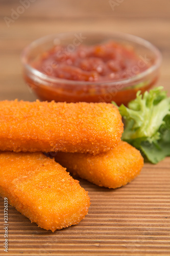 Fish sticks, fast food with tomatoe sauce. Rustic wooden background.
